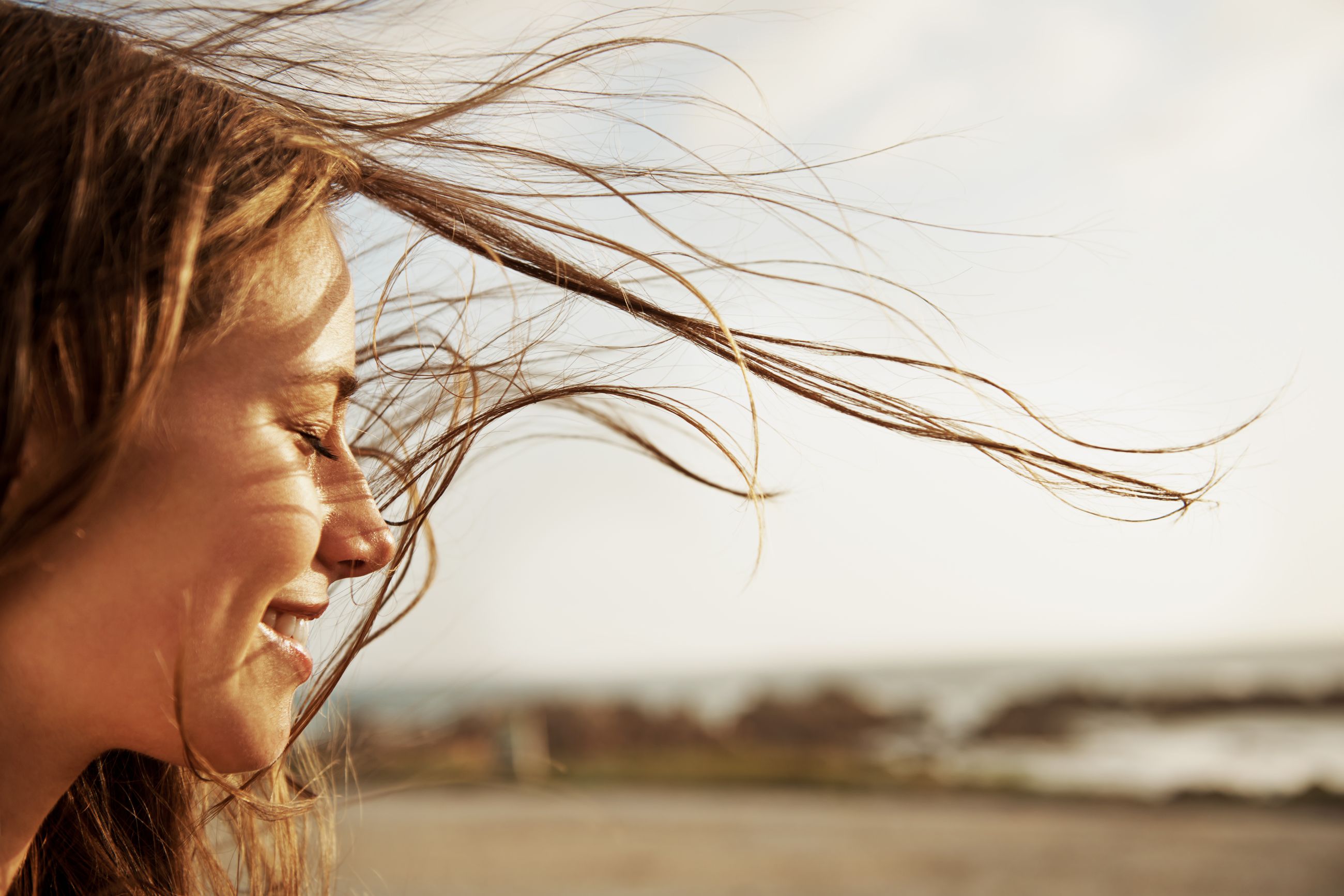 Mujer sonriendo frente al mar, con el pelo al viento